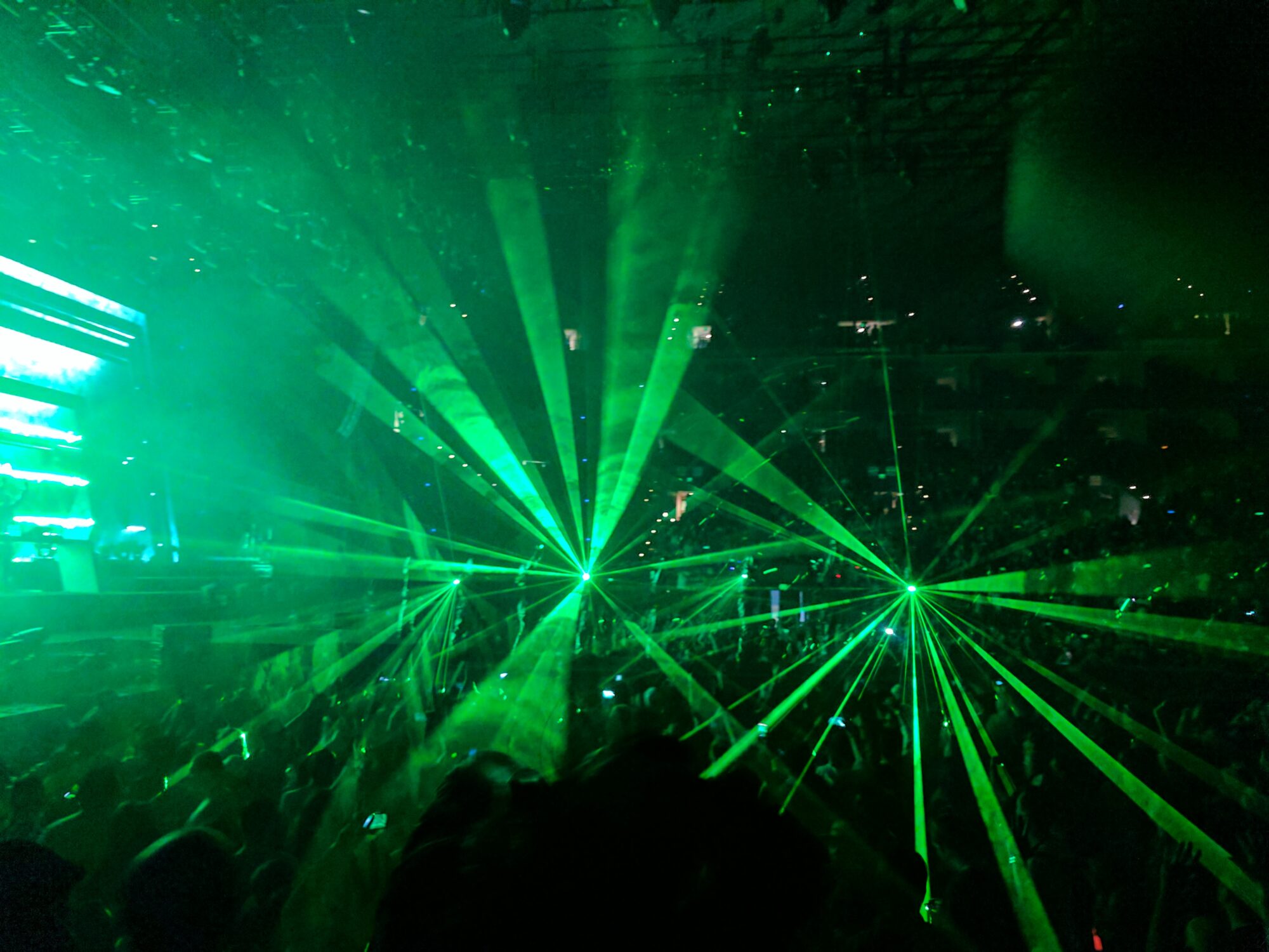 A laser show with green lasers over a sizable crowd.
